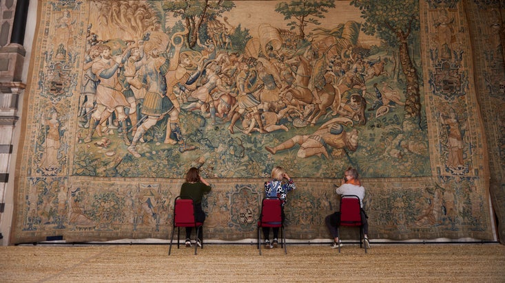 Three women sat down working on the Hardwick Tapestry in the Long Gallery at Hardwick Hall, Derbyshire